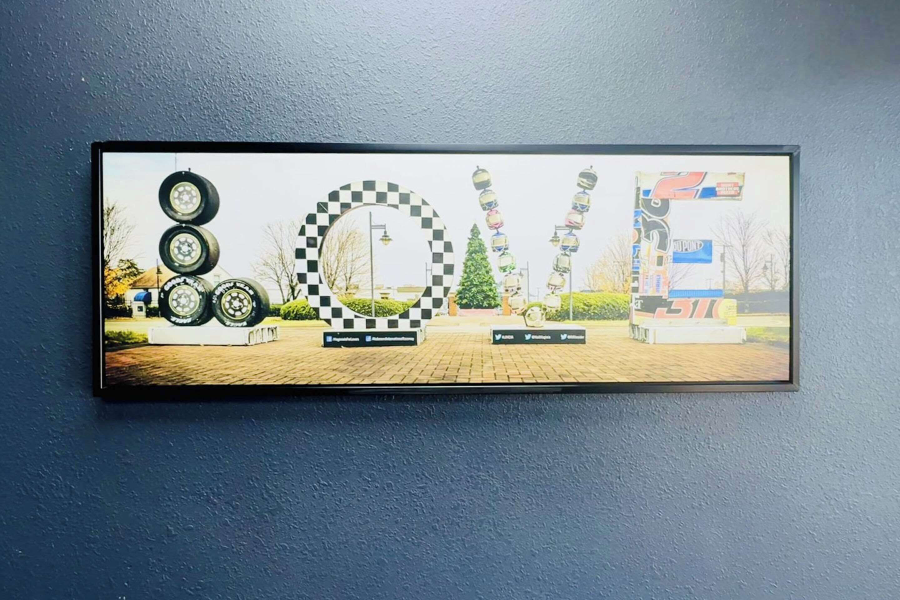 A framed artwork featuring tires, a checkered flag, and a racing car.