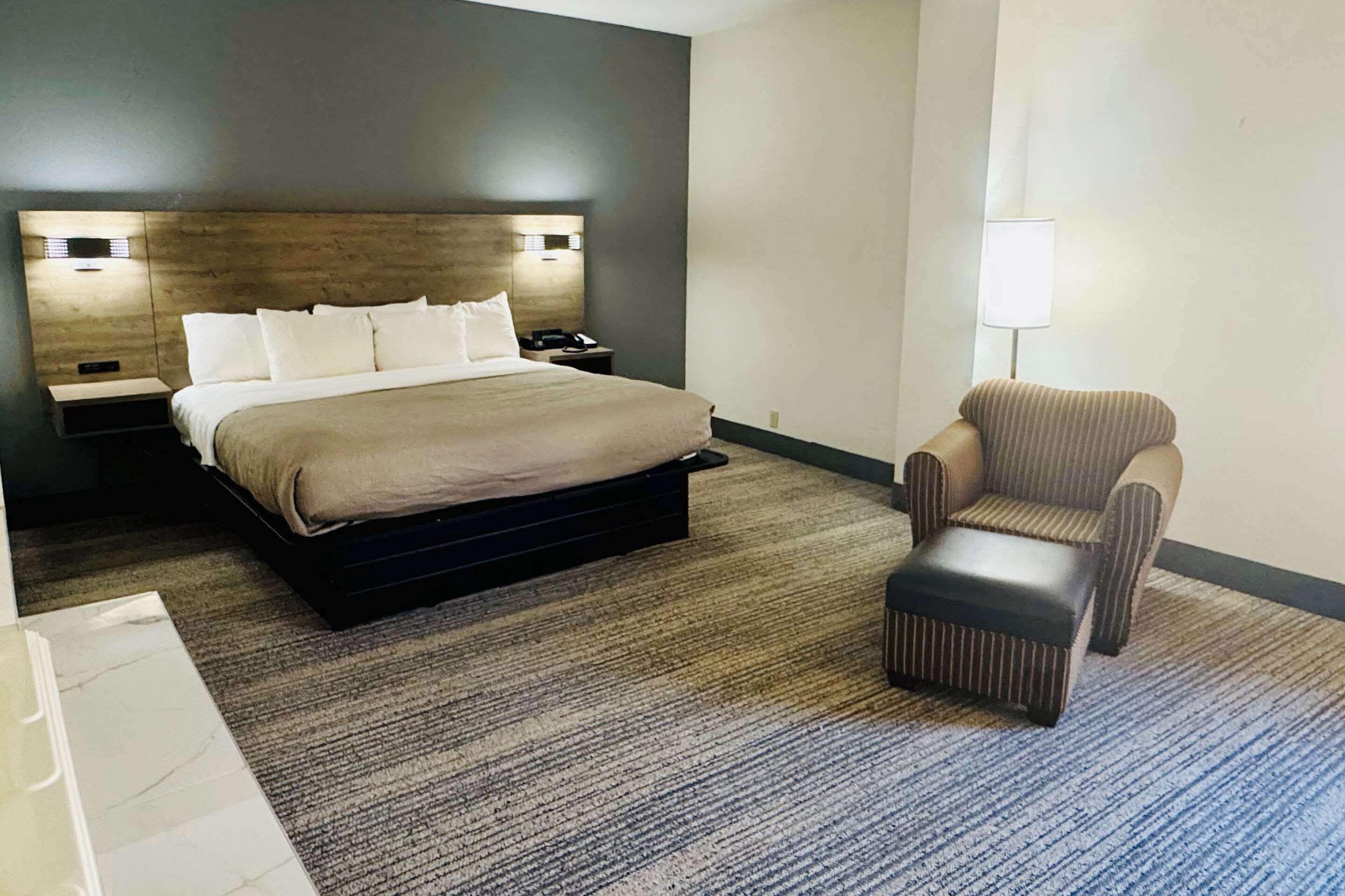 A hotel room with a large bed, a bedside table with a lamp, and a striped armchair.