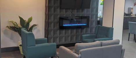 Un salon moderne comprenant deux fauteuils, un téléviseur à écran plat et une grande plante en pot.
