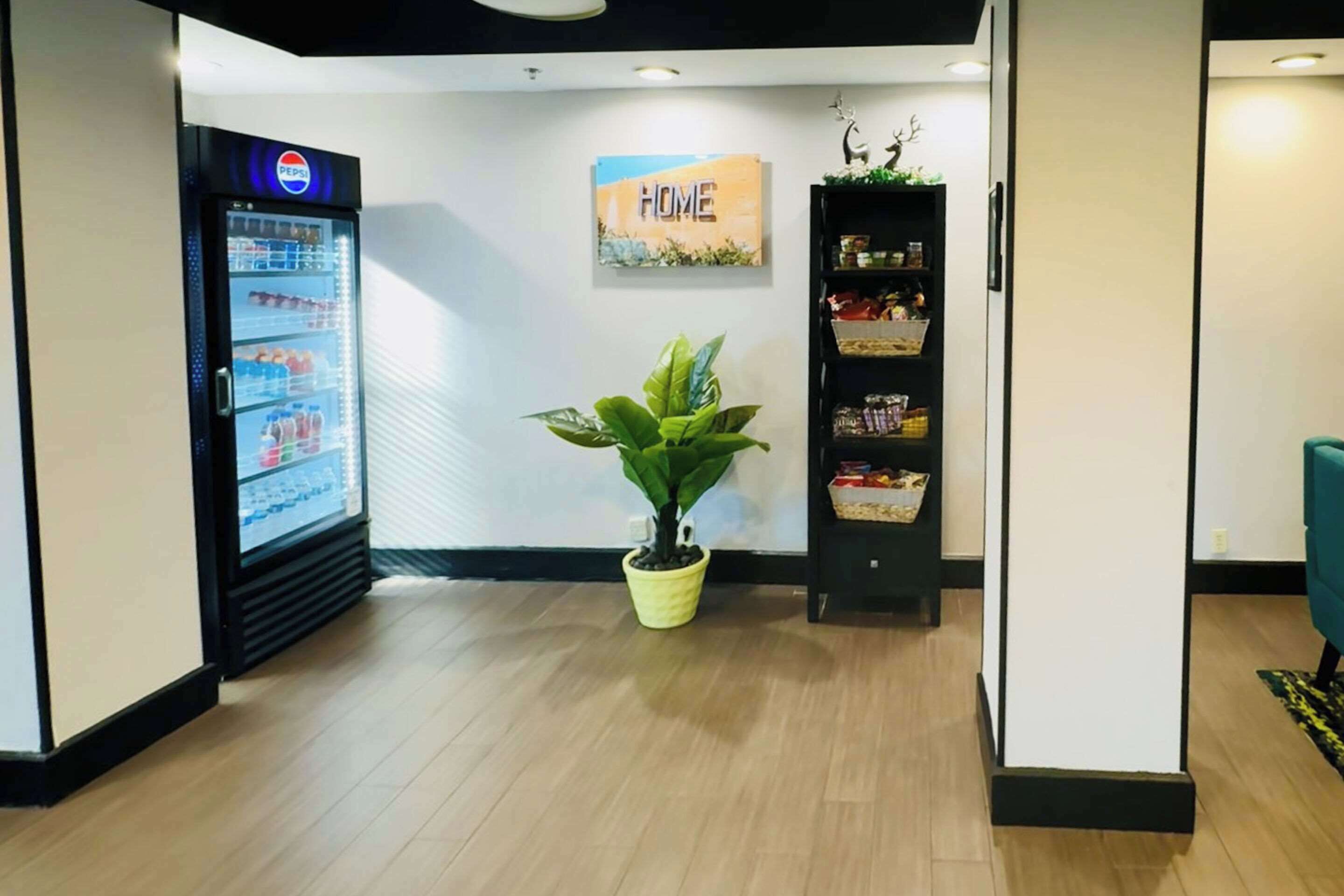 A lobby with a Pepsi refrigerator, a potted plant, a 'HOME' sign, and a bookshelf.