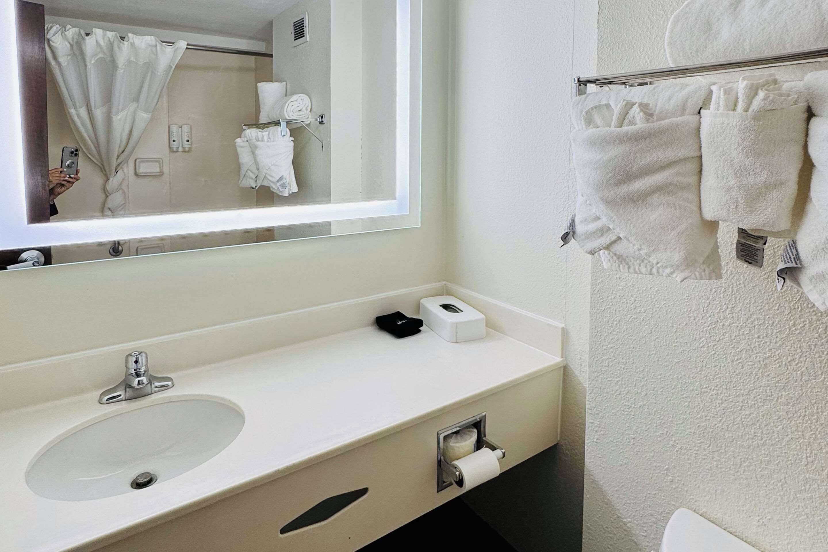 A bathroom with a sink, mirror, towel rack, and a toilet paper holder.