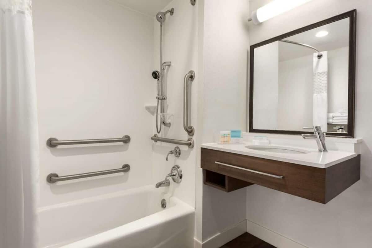 A modern bathroom with a white bathtub, a vanity with a mirror, and grab bars for accessibility.