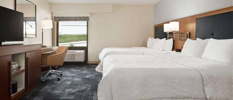 A hotel room with a large bed, a desk with a TV, a chair, and a window with a view of the outdoors.