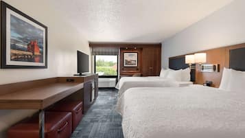 Quarto de hotel com duas camas, uma mesa, uma televisão e janela com vista.