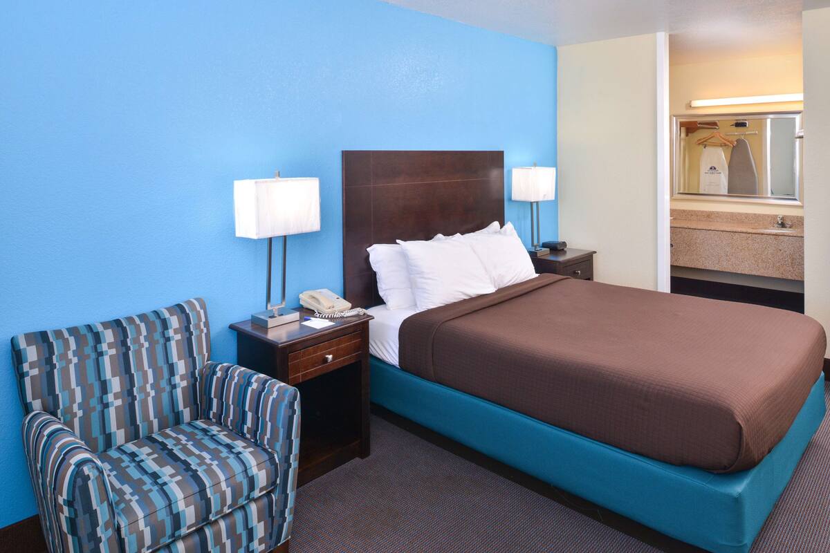 A hotel room with a large bed, a chair, a nightstand with a phone, and a mirror.