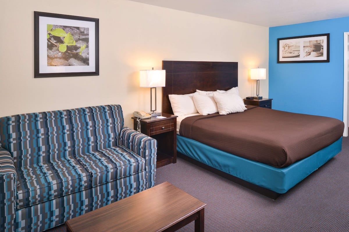 A hotel room with a bed, a sofa, two bedside tables, and two lamps.