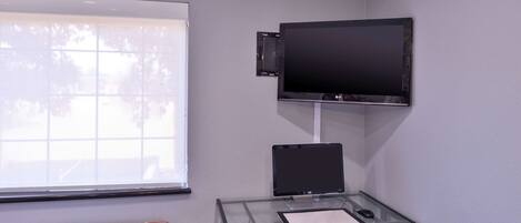 Un espacio de oficina moderno con escritorio de vidrio, computadora y televisor de pantalla plana montado.