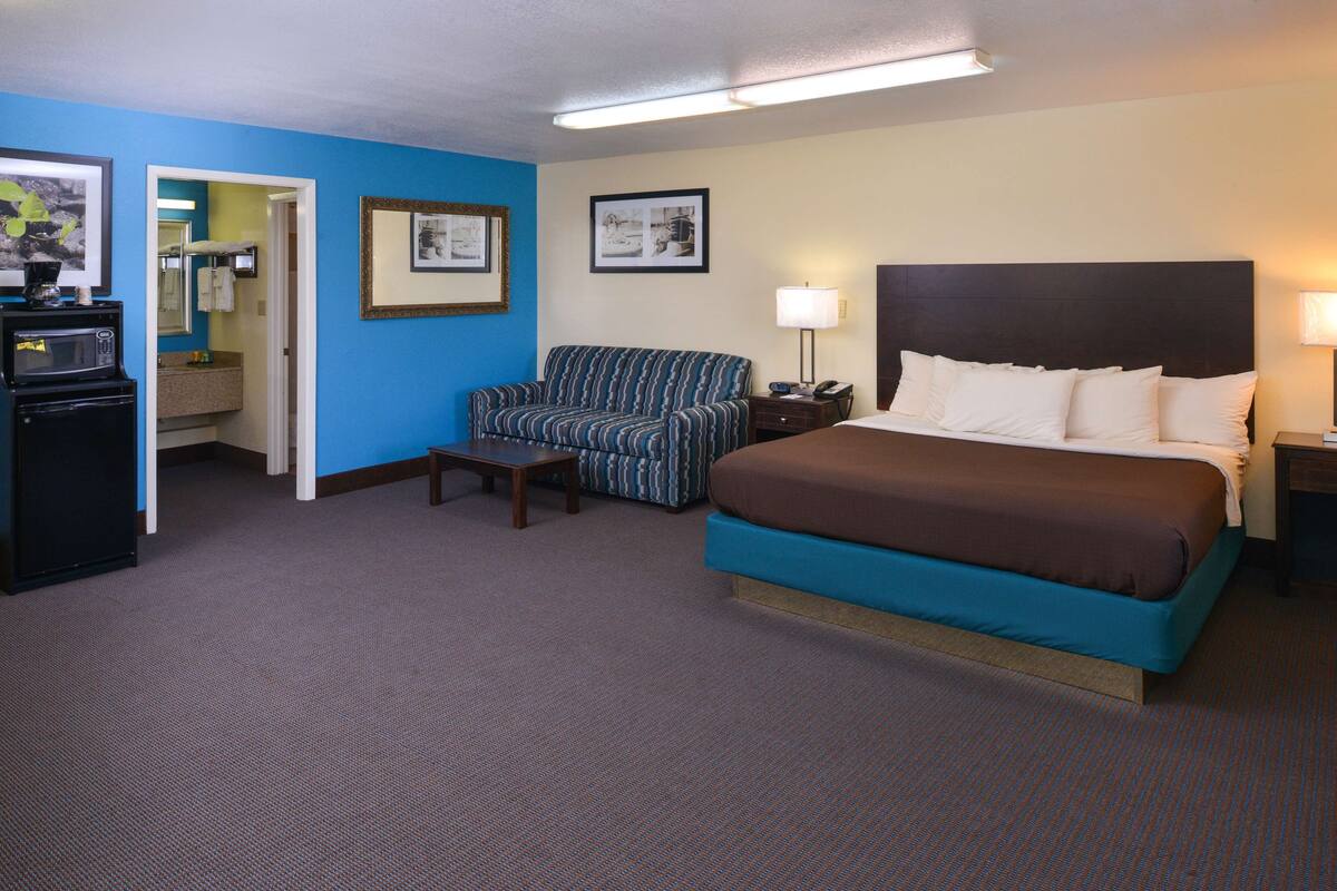 A hotel room with a bed, a chair, a desk, a microwave, and a bathroom visible through an open door.