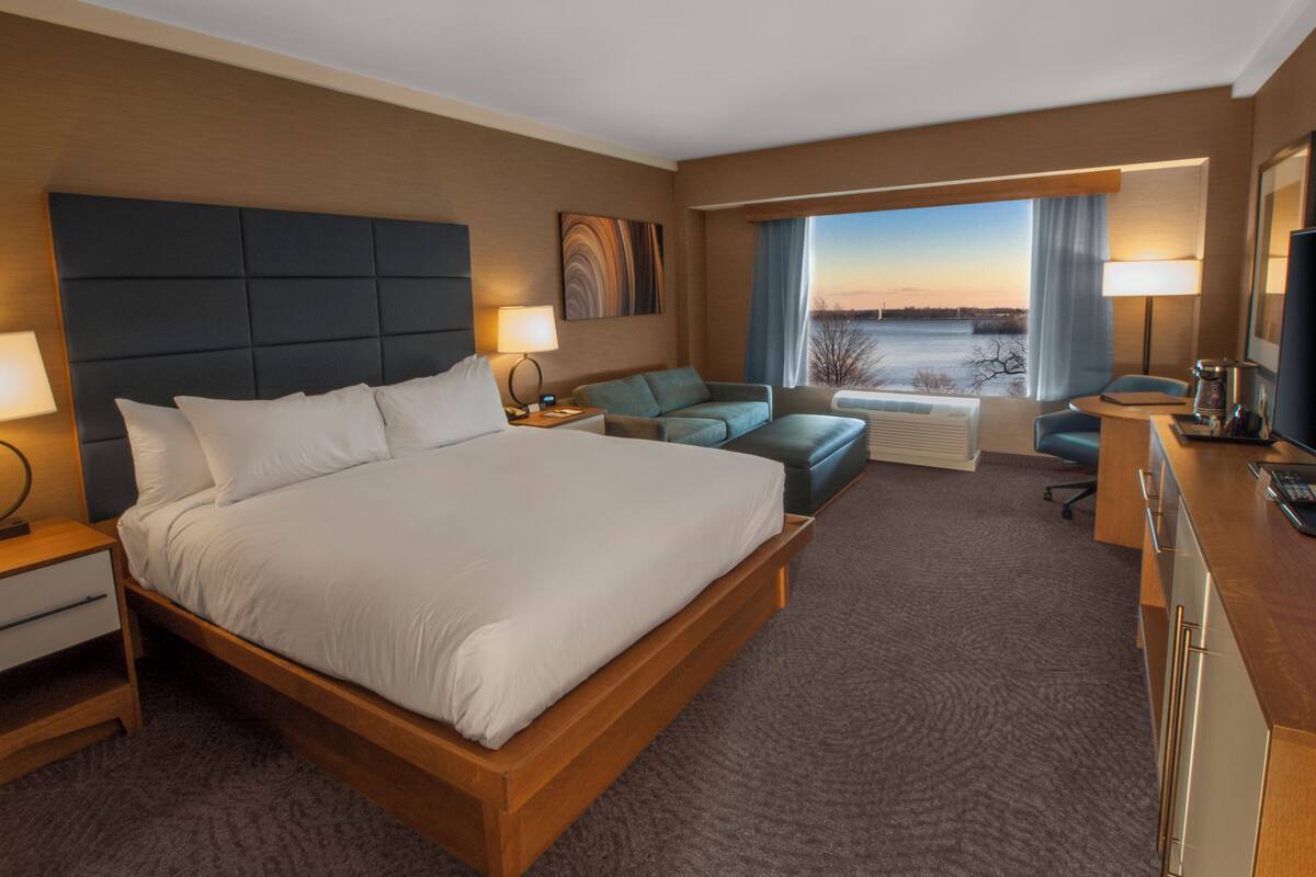 A hotel room with a large bed, a sofa, a desk, and a view of the outdoors.