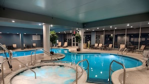 An indoor swimming pool with multiple lanes, lounge chairs, and a hot tub area.