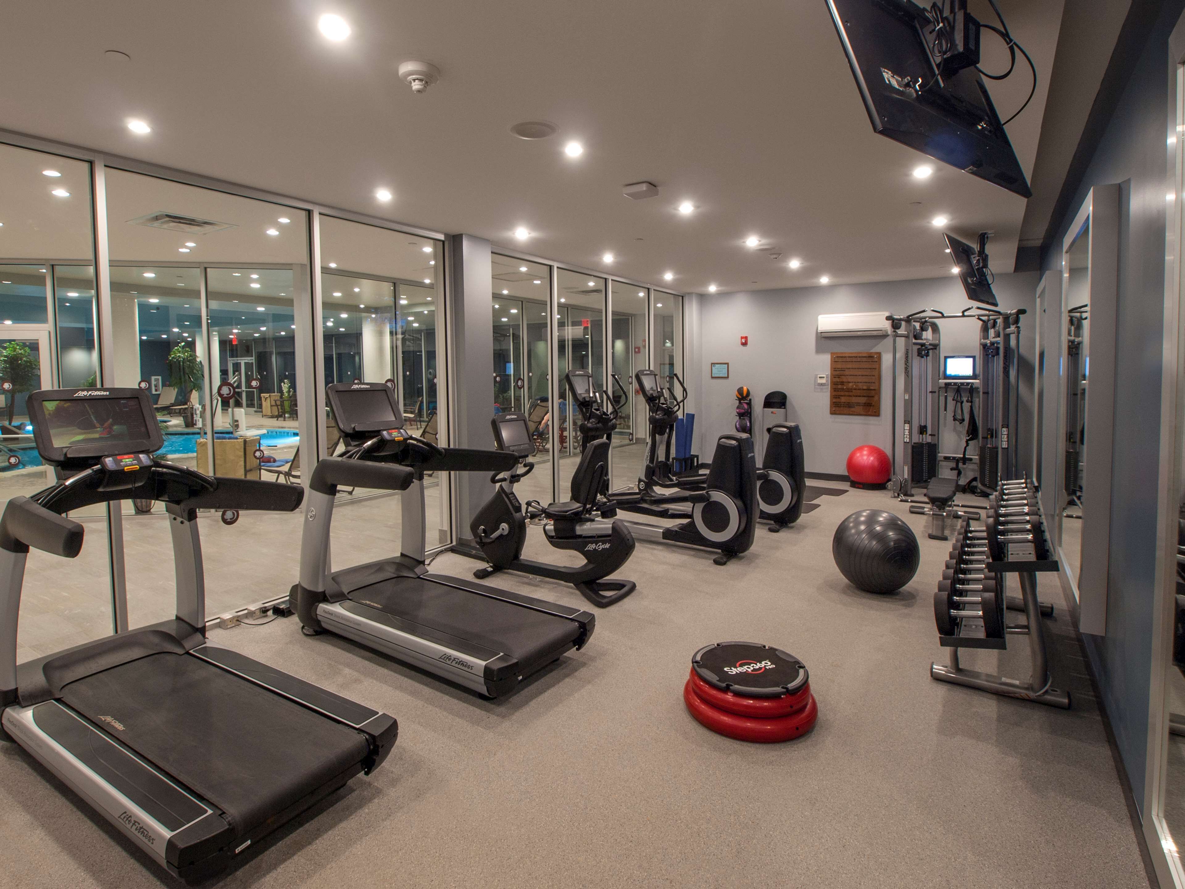 A modern gym with treadmills, elliptical machines, and weight equipment.
