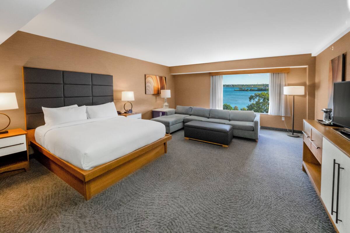 A hotel room with a large bed, a sofa, a TV, and a view of the water.