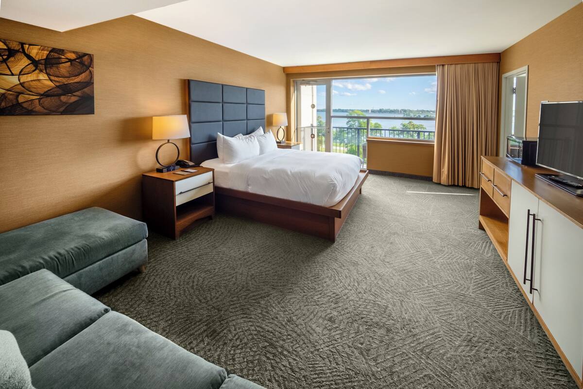 A hotel room with a large bed, a sofa, a desk with a TV, and a view of the outdoors.