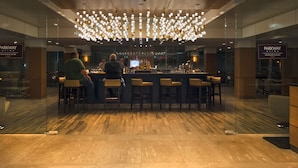 A modern bar area with a central light fixture, wooden flooring, and bar stools.