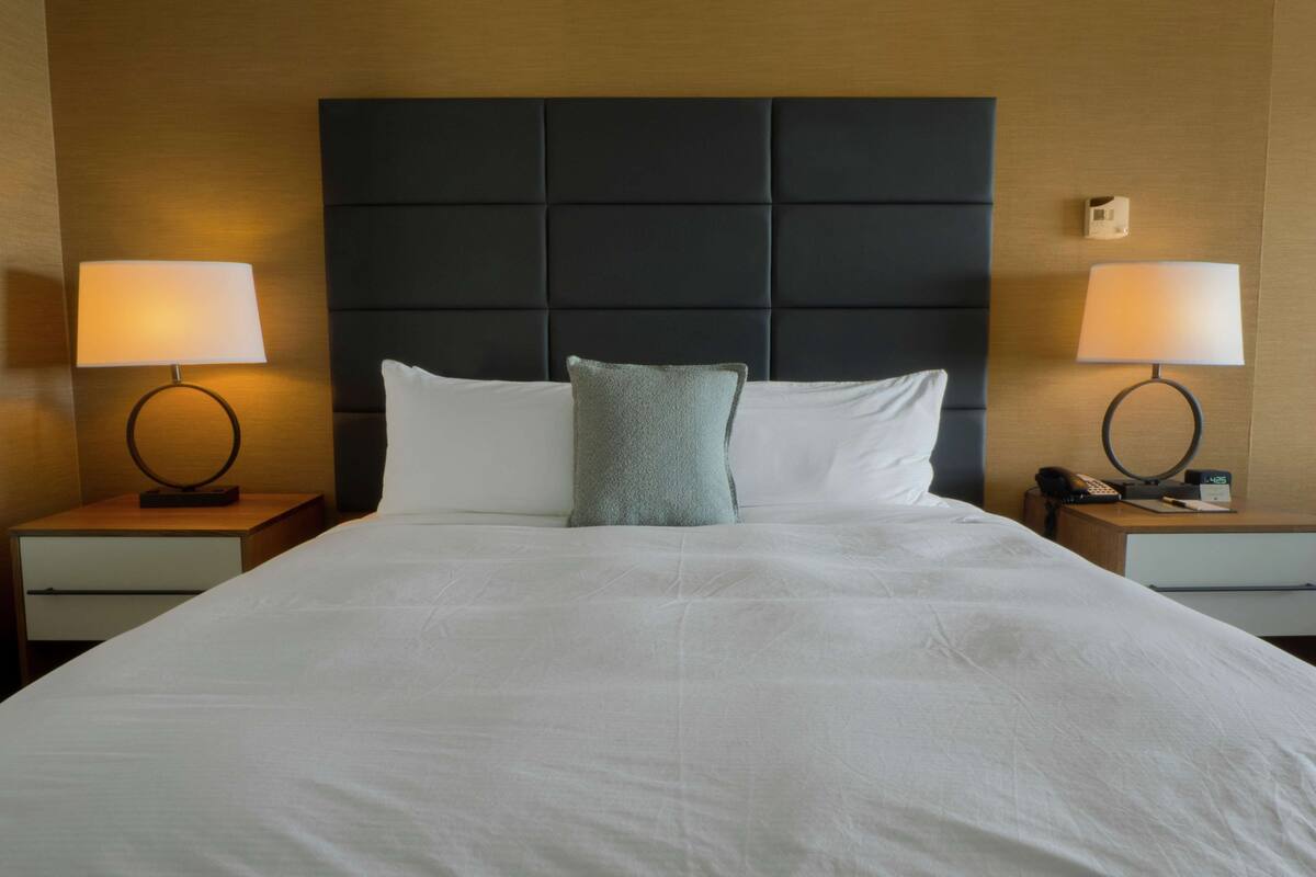 Een hotelkamer met een groot bed, twee nachtkastjes en een hoofdeinde.