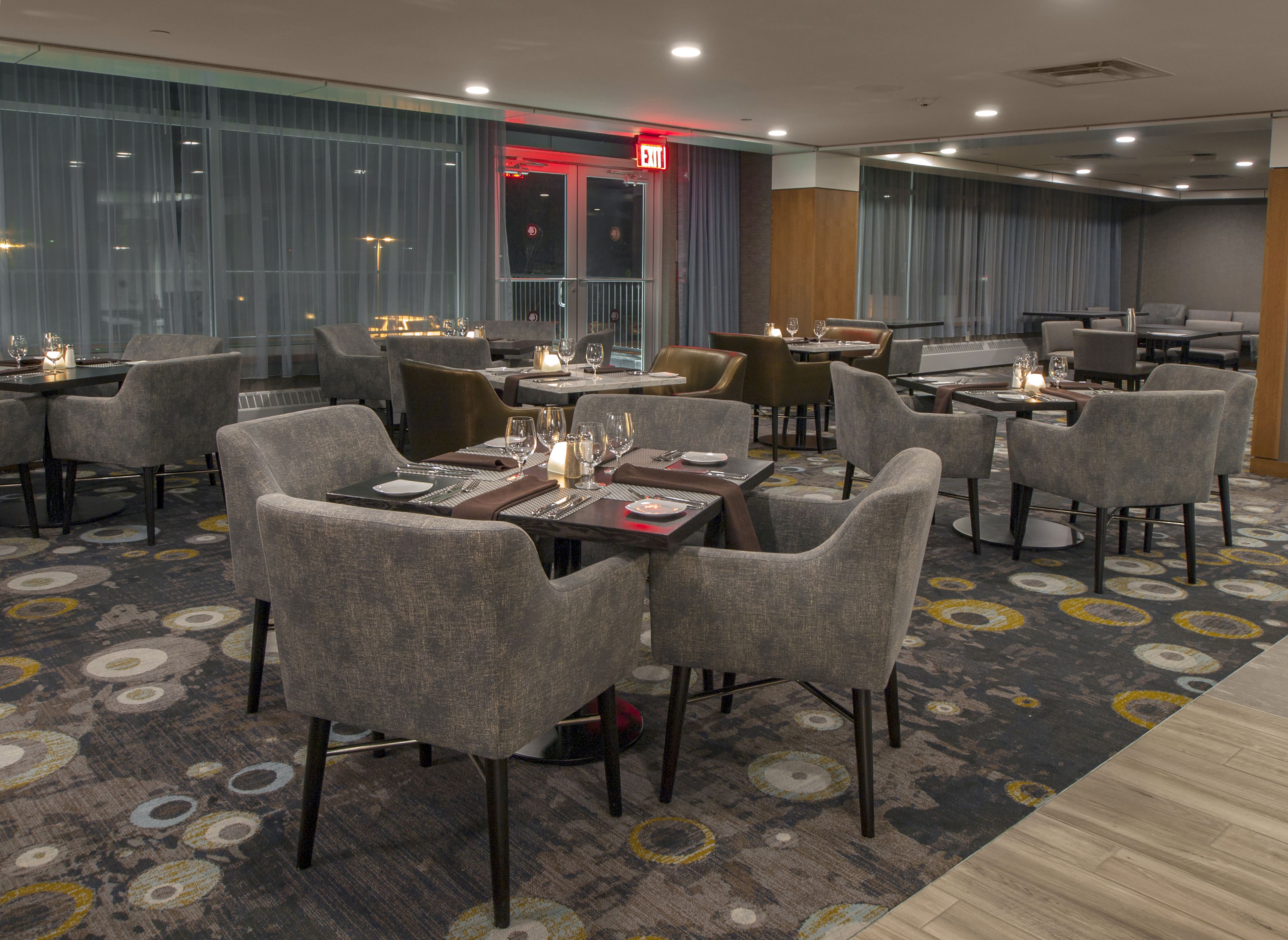 A modern restaurant with multiple dining tables and chairs, equipped with candles and wine glasses.