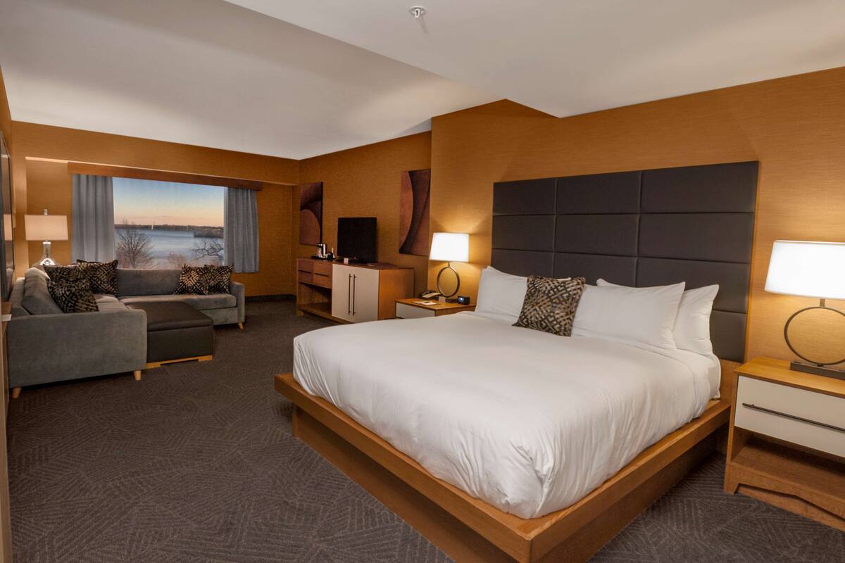 A hotel room with a large bed, a sofa, a desk, and a TV.