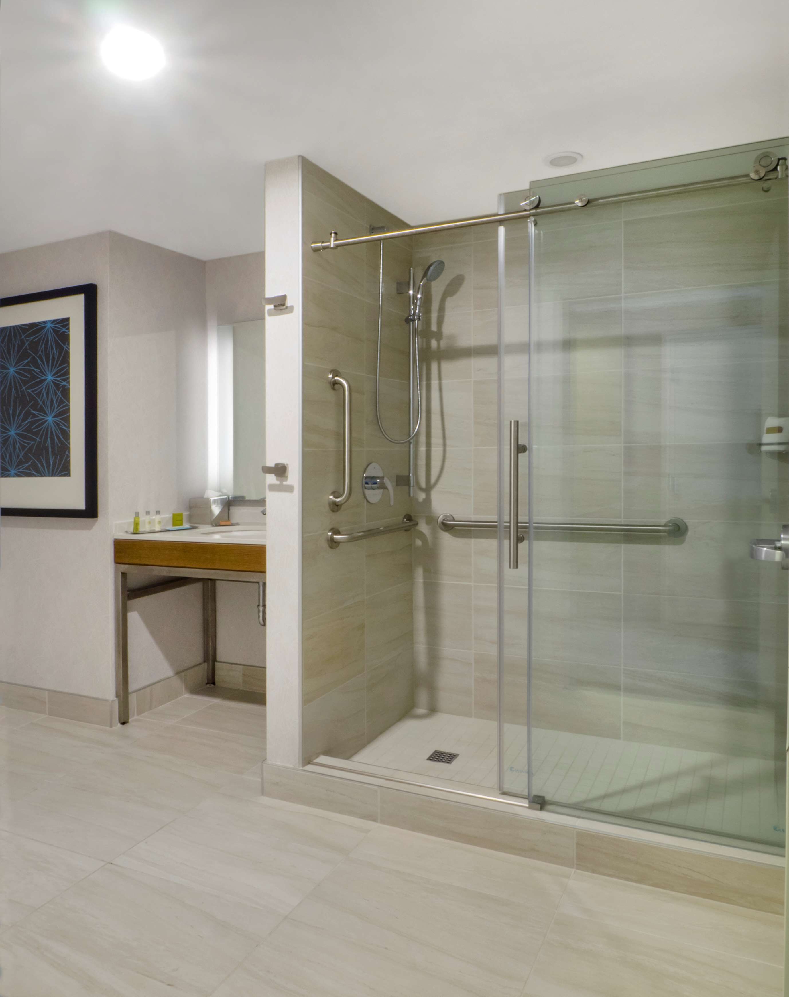 A modern bathroom with a glass-enclosed shower, a vanity with a sink, and a framed abstract artwork on the wall.