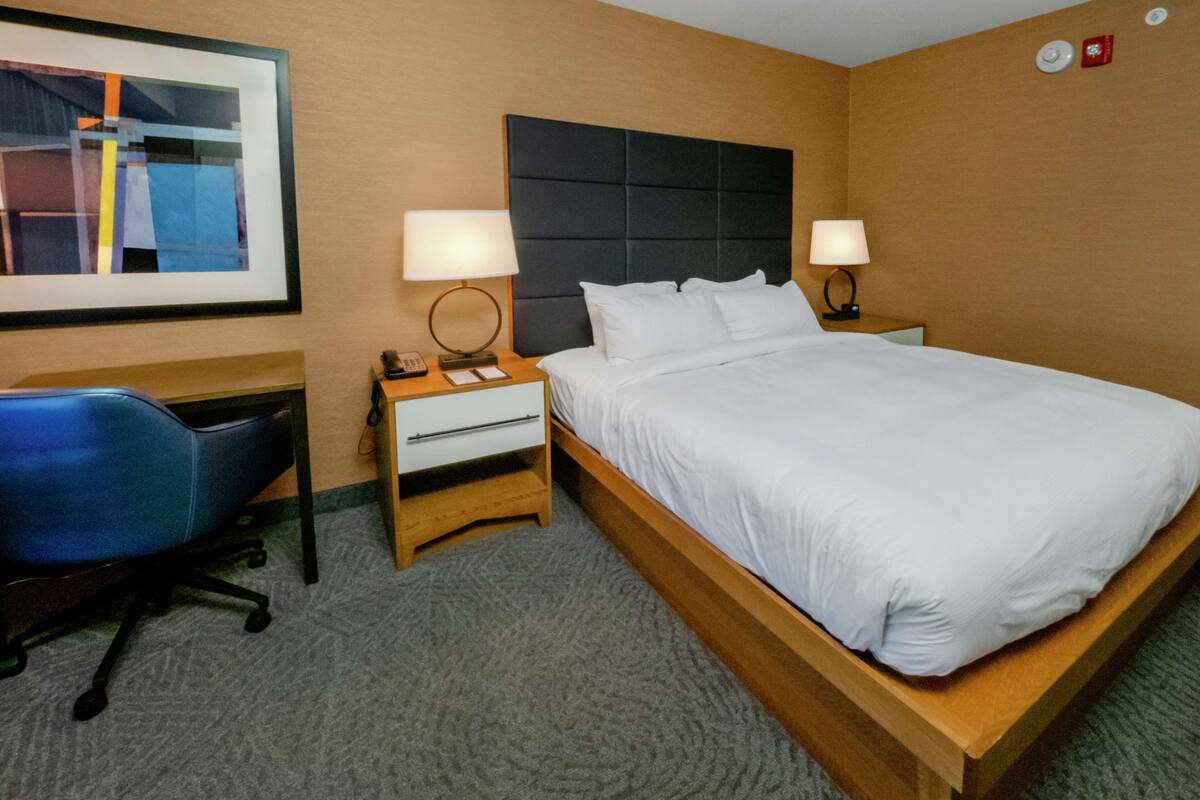 A hotel room with a bed, two bedside tables with lamps, a desk, and a chair.