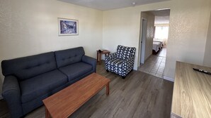 A living room with a dark grey sofa, a patterned armchair, and a wooden coffee table. A framed picture hangs on the wall. - Days Inn by Wyndham San Marcos (San Marcos)