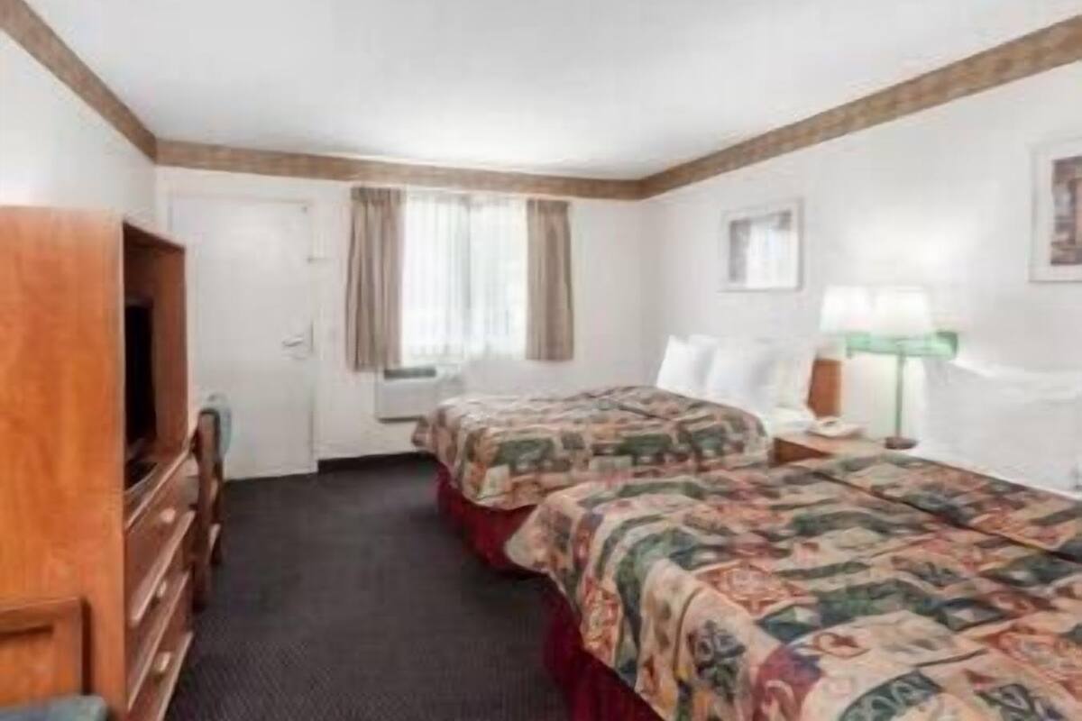 A hotel room with two beds, a wooden dresser, a television, a lamp, and a window with curtains.