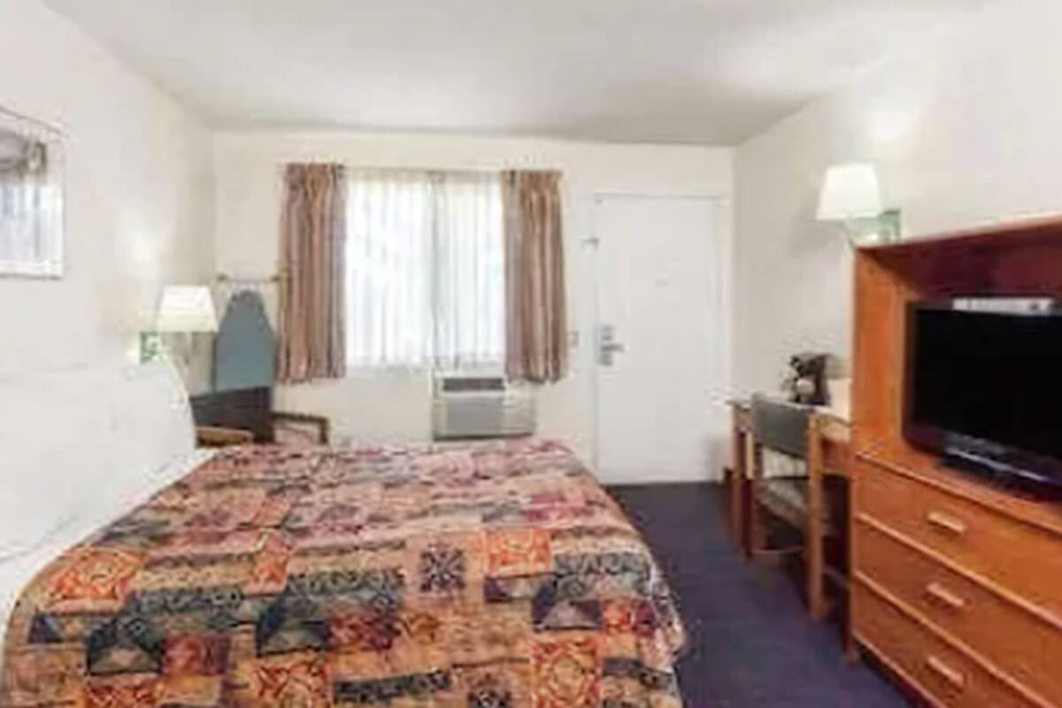 A hotel room with a bed, a television, a desk, and a dresser.