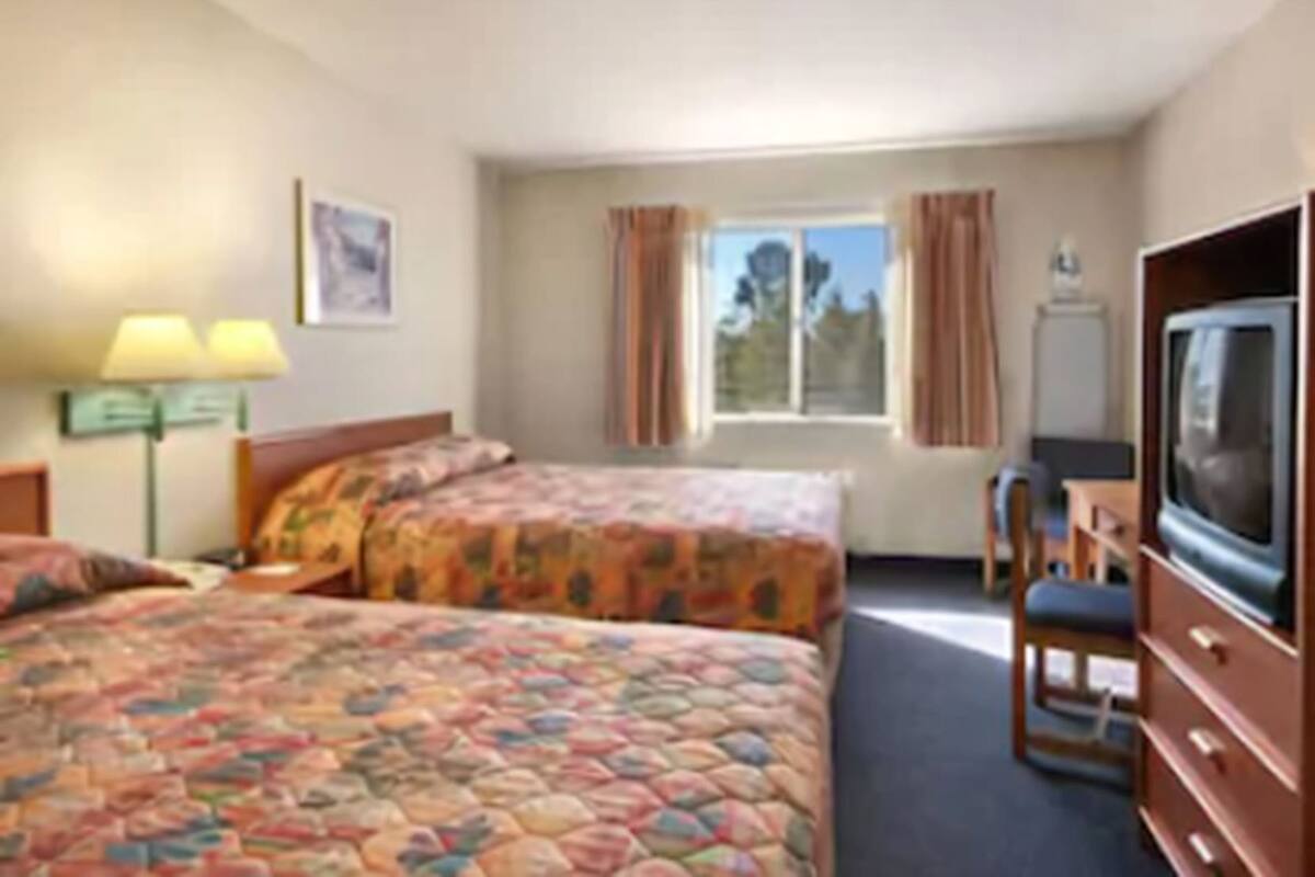 A hotel room with two beds, a desk, a television, and a window with curtains.