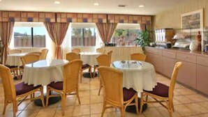 A dining area with round tables and chairs, a kitchen area with cabinets, and a window with curtains. - Days Inn by Wyndham San Marcos (San Marcos)