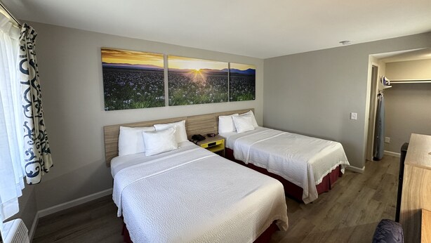 A hotel room with two beds, a large window with a sunset view, and a wooden floor. - Days Inn by Wyndham San Marcos (San Marcos)