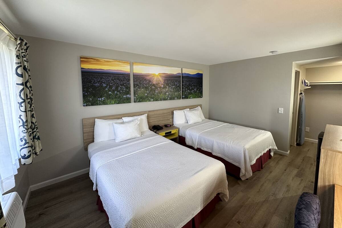 A hotel room with two beds, a large window with a sunset view, and a wooden floor.