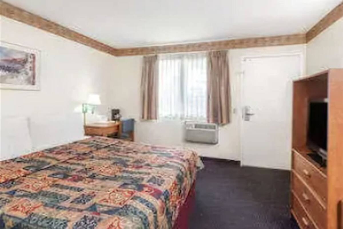 A hotel room with a bed, a dresser, a television, a window with curtains, and a painting on the wall.