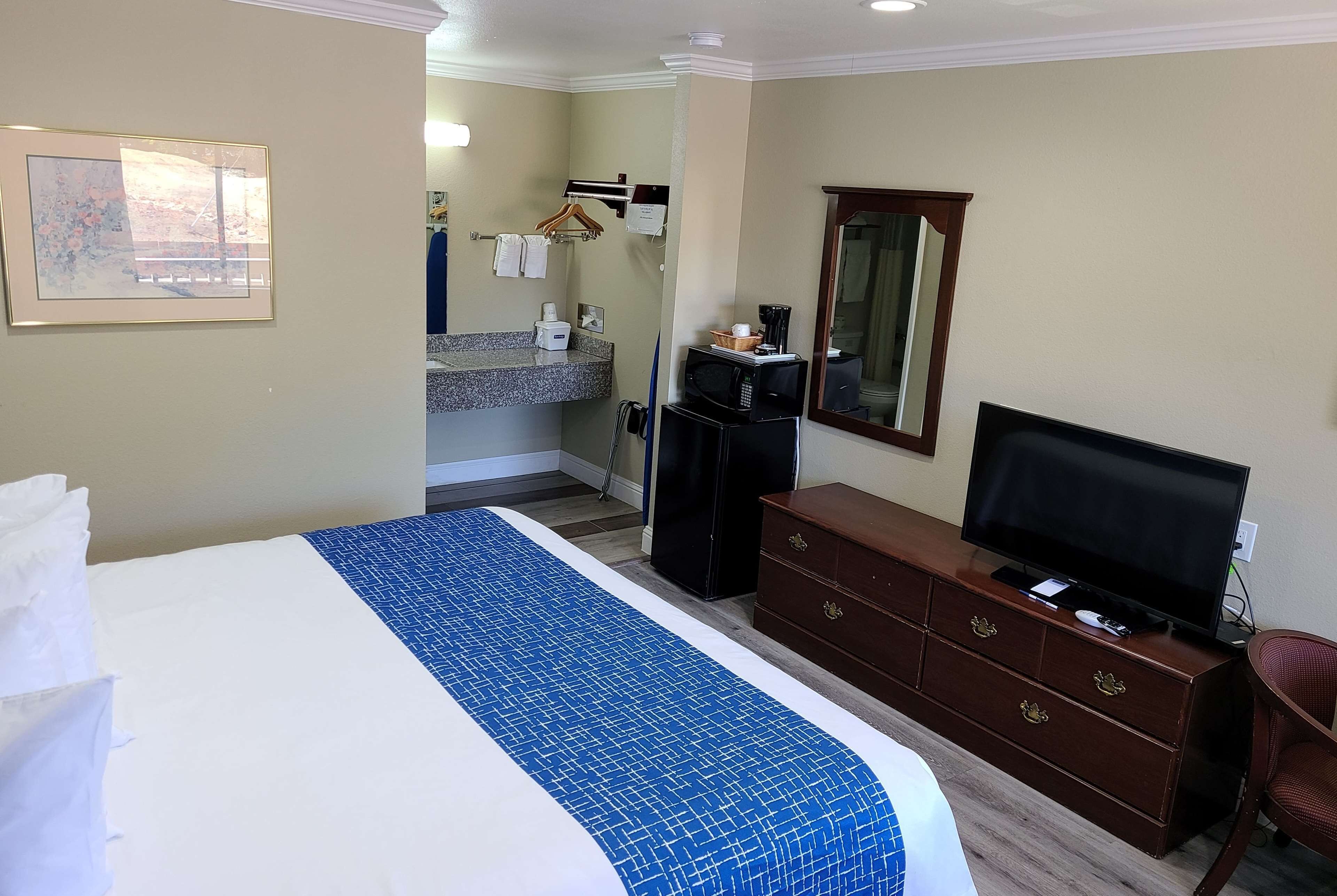 Habitación de hotel con una cama grande, un tocador, un televisor, un microondas y un baño a la vista.