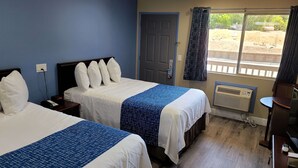 Habitación de hotel con dos camas, ventana con vistas al exterior, puerta y una mesita con una silla.