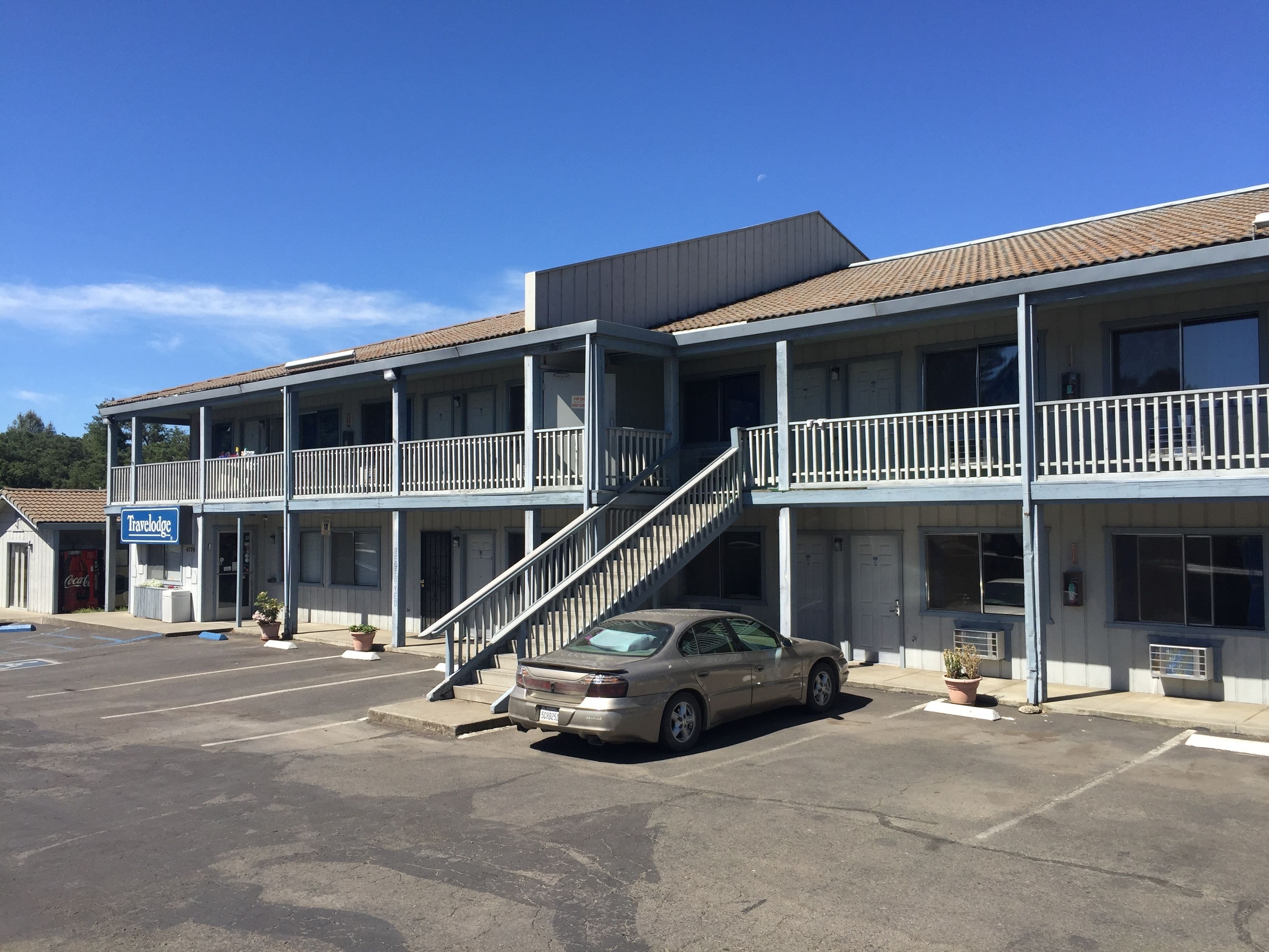 A Travelodge motel with a two-story structure, a parking lot, and a car parked in front.