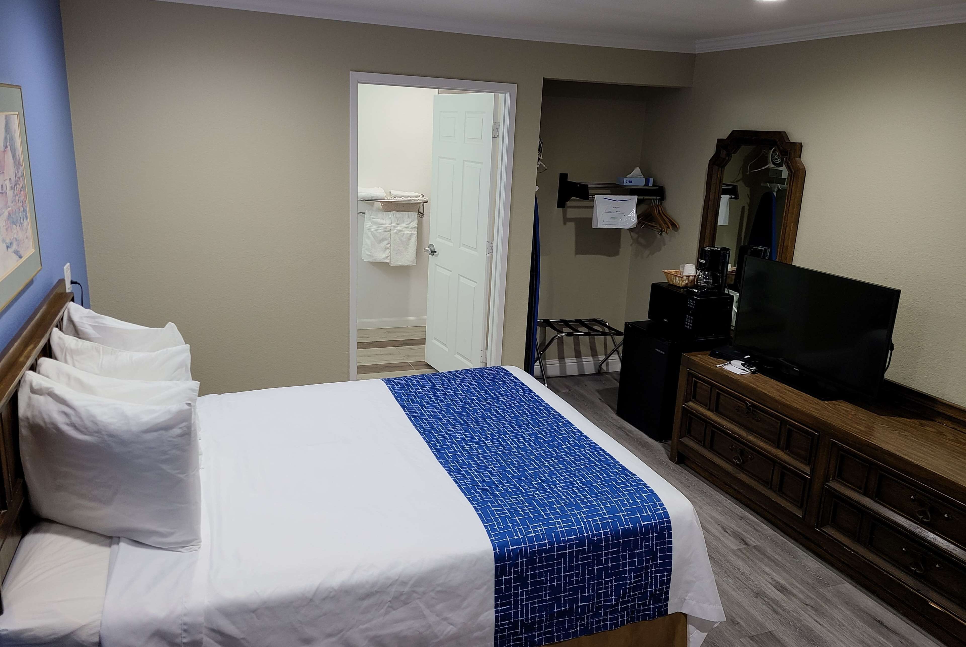 Une chambre d’hôtel comprenant un lit, une commode, un téléviseur et une porte donnant sur une salle de bain.