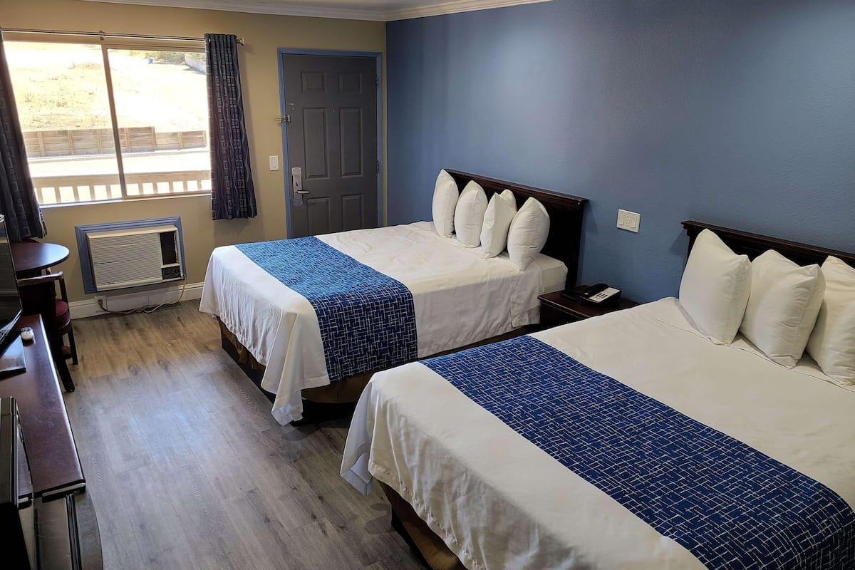 Une chambre d’hôtel avec deux lits, un bureau, une chaise, une télévision et une fenêtre avec des rideaux.