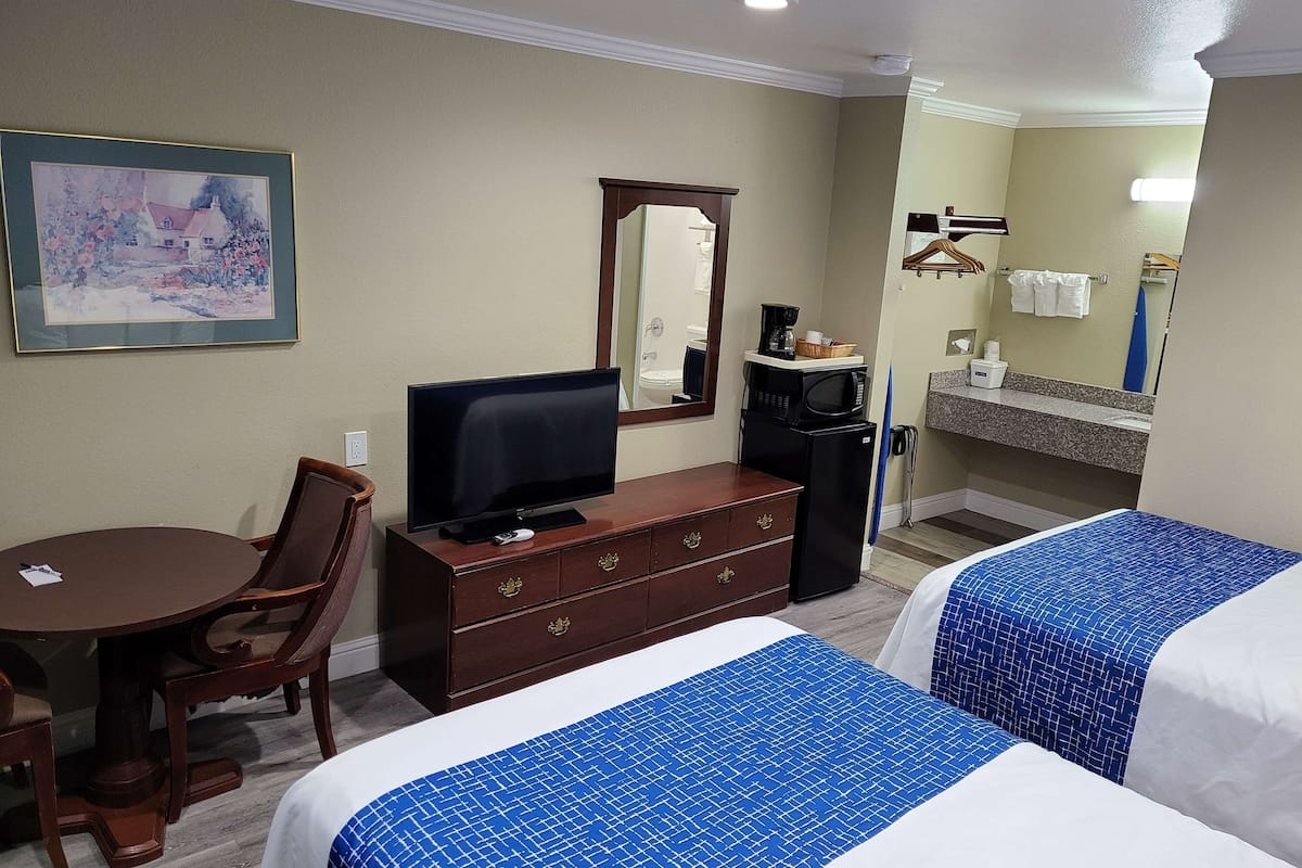 Une chambre d’hôtel équipée d’une table à manger, d’un téléviseur, d’une commode, d’une machine à café et de deux lits avec une literie bleue et blanche.