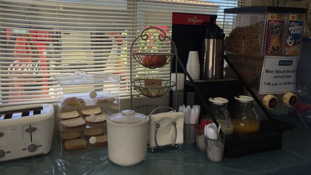 Una zona de desayuno con una tostadora, pan, una cafetera y un cartel que indica los horarios del servicio de desayuno.