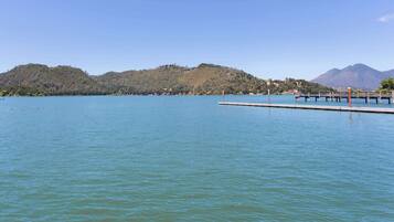 A calm lake with a pier extending into the water, surrounded by hills and a clear sky.