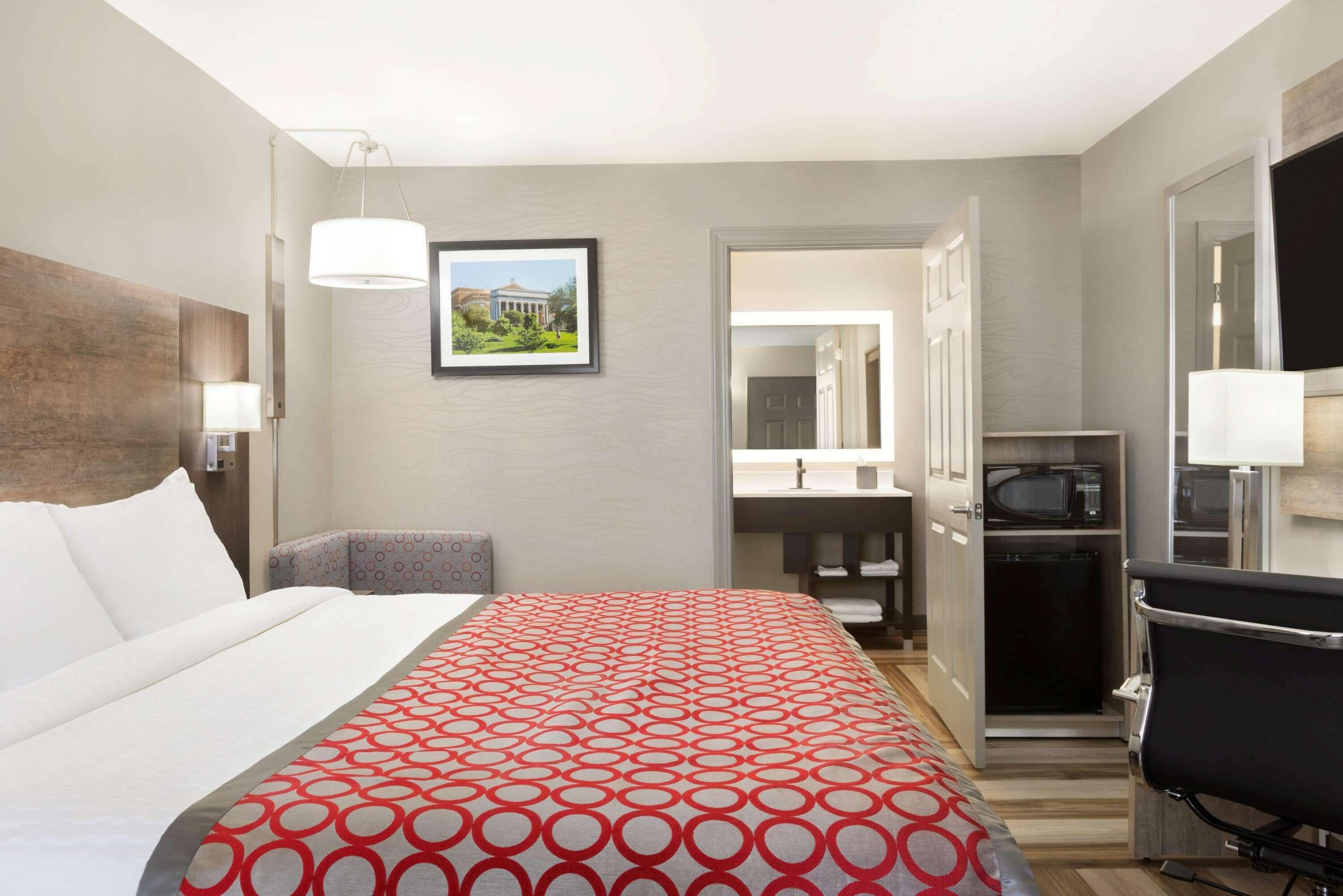 A hotel room with a bed, a desk, a chair, a microwave, and a bathroom visible through an open door.