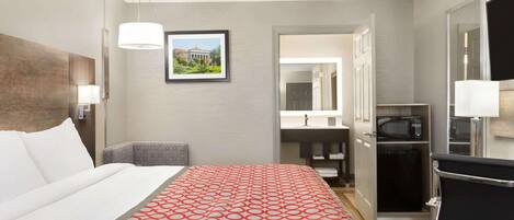 A hotel room with a bed, a desk, a chair, a microwave, and a bathroom visible through an open door.