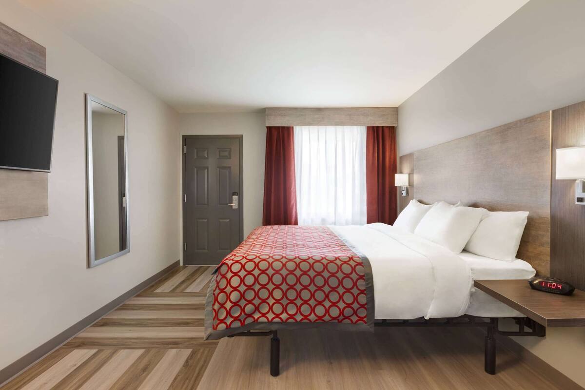 A hotel room with a bed, a TV, a door, and a window with curtains.