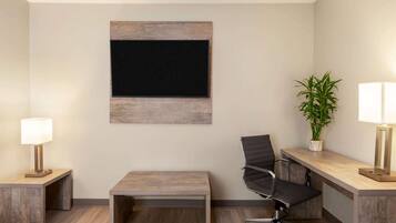 A modern office space with a wooden desk, a black office chair, a small table, a potted plant, and a wall-mounted blackboard.