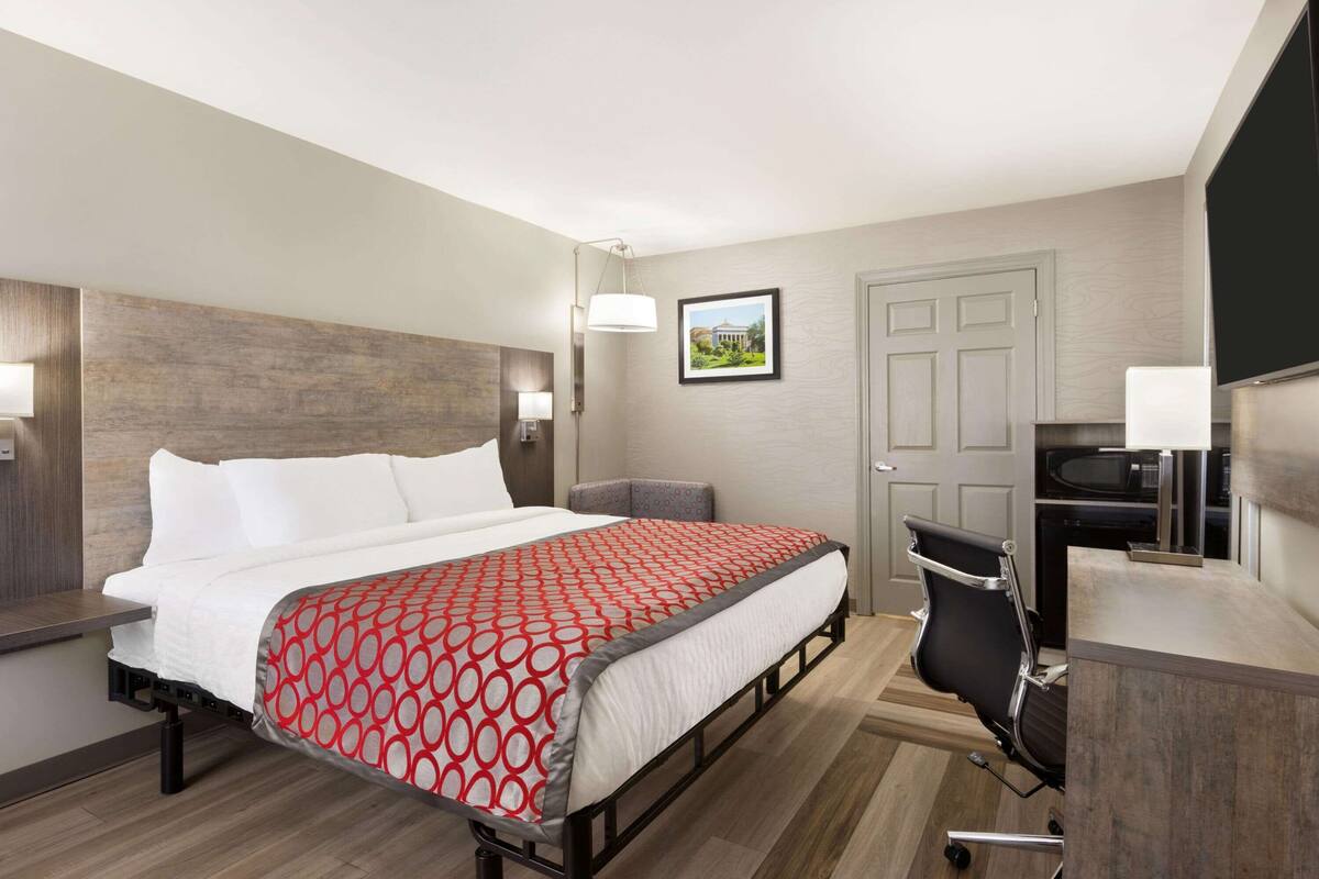 A hotel room with a bed, a desk with a chair, a television, and a door.