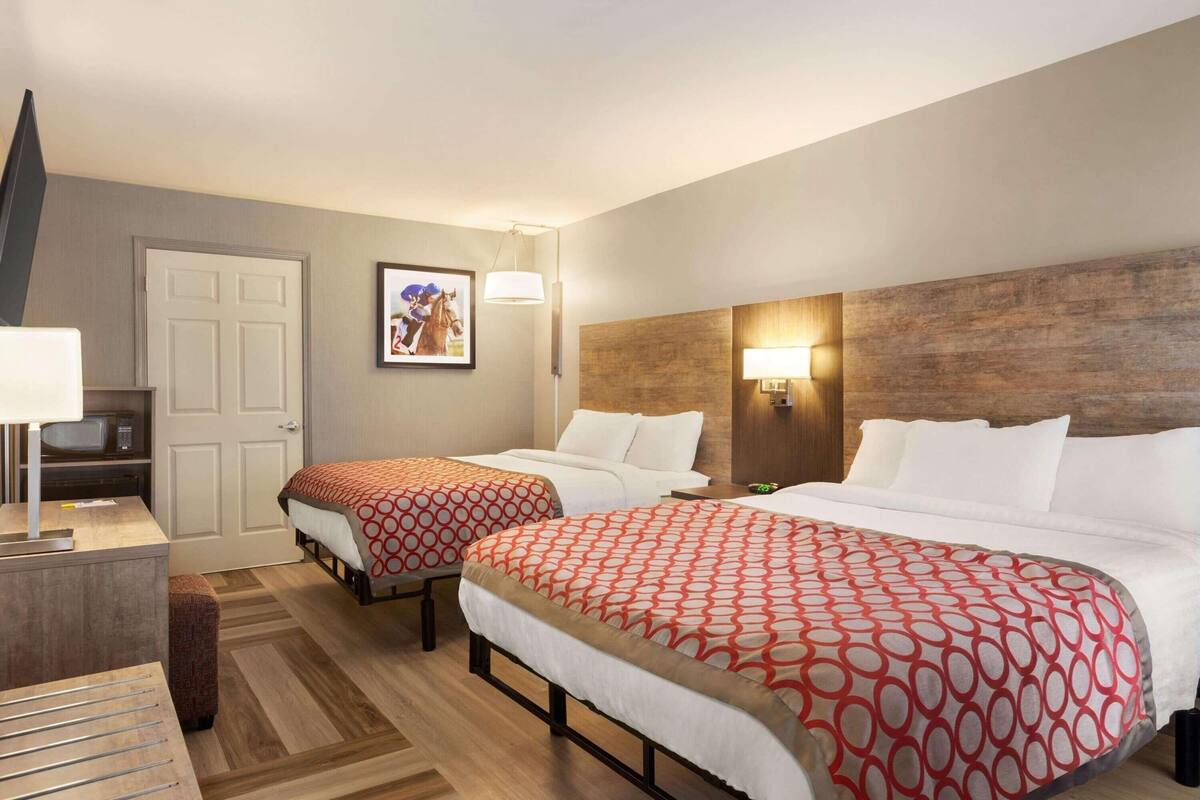 A hotel room with two beds, a TV, a desk, and a wooden headboard.