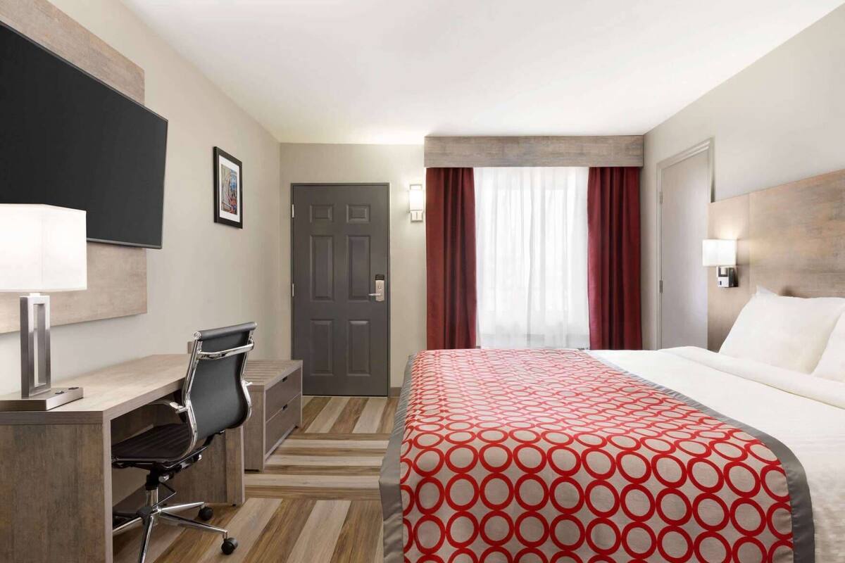 A hotel room with a bed, desk, chair, and a door.