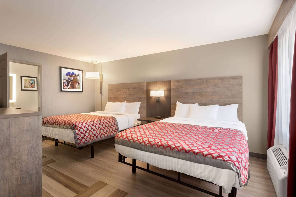 A hotel room with two beds, a desk, a mirror, and a wall-mounted lamp.