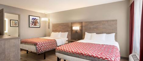 A hotel room with two beds, a desk, a mirror, and a wall-mounted lamp.