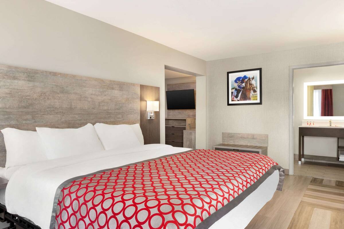A hotel room with a large bed, a TV, a painting, and a bathroom.