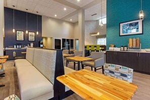 A modern cafe with seating areas, wooden tables, and a kitchen in the background.